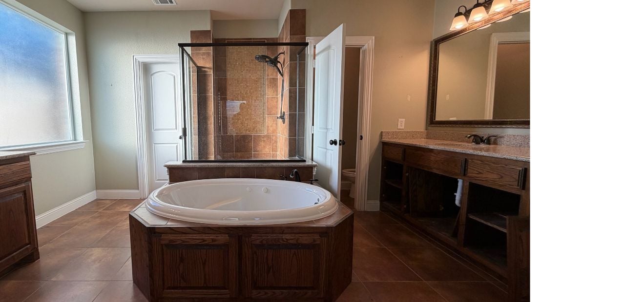 Before master bathroom remodel in North Dallas with brown tile, dark wood vanities, built-in soaking tub, and framed glass shower
