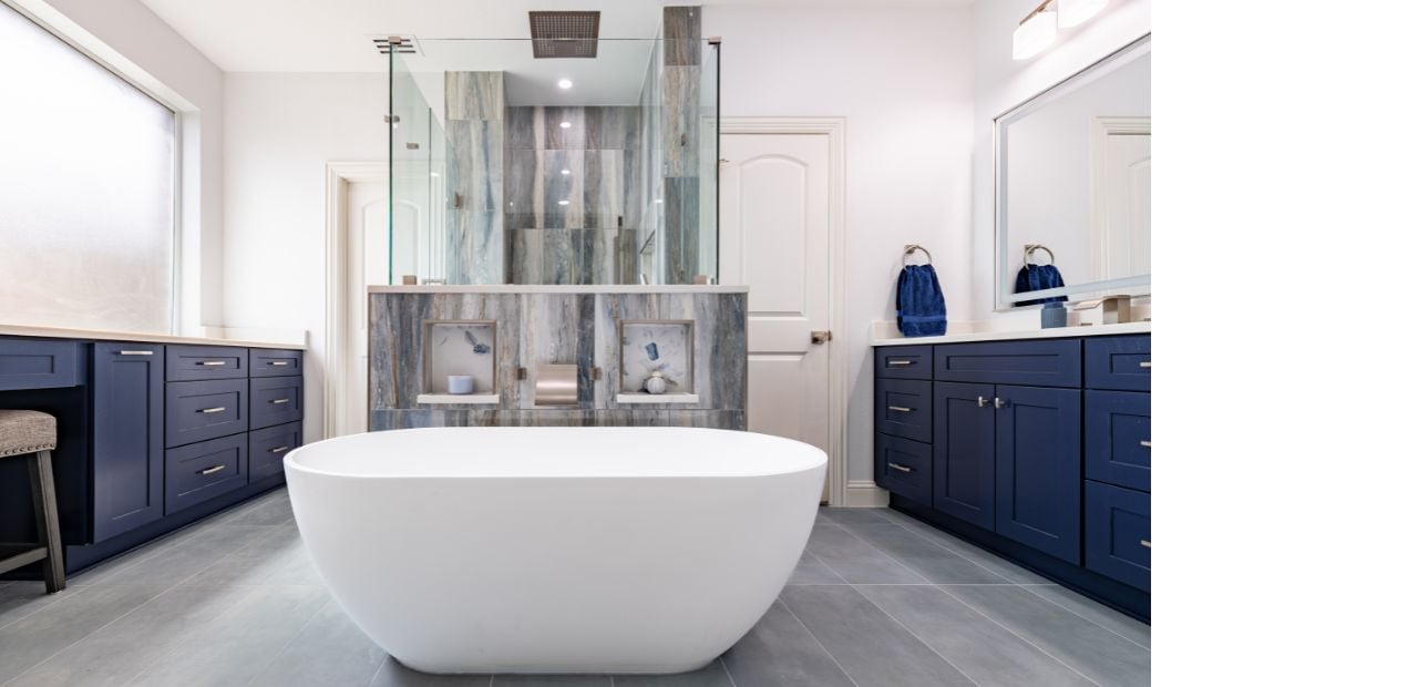Completed luxury bathroom renovation in North Dallas featuring a white freestanding tub, custom blue cabinetry, walk-in shower, and upscale modern finishes