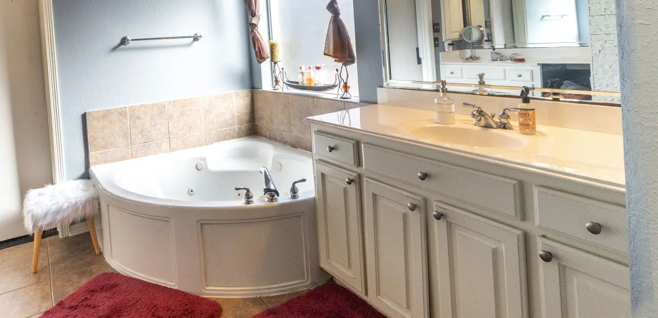 Outdated full bath with beige single vanity and corner jacuzzi tub